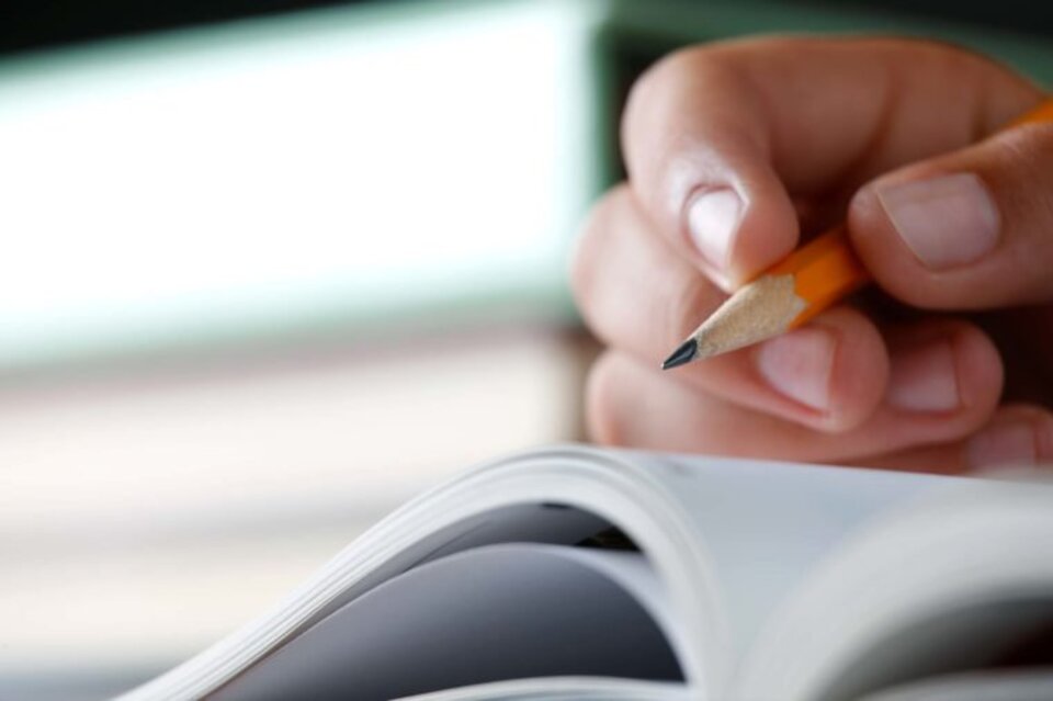 Hand holding pencil over notebook.